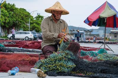 被海風鏤刻出 滿面風霜的漁工們，在漁港邊熟練靈巧地補著破網。（莊坤儒攝） 