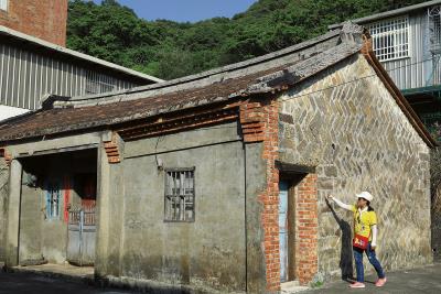 協會總幹事蔡彩芳指著百年古厝 「瑪鋉居」，牆面上的「人字砌」， 象徵人丁興旺。